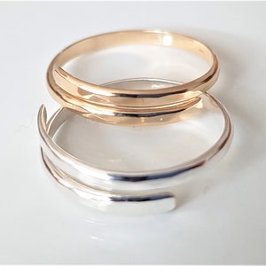 Peut inclure: Deux bagues simples et minimalistes, l'une en argent et l'autre en or, sont empilées l'une sur l'autre. Les bagues sont toutes deux simples et lisses, sans ornements.