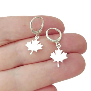 Peut inclure: Une paire de boucles d'oreilles créoles argentées avec des pendentifs en forme de feuille d'érable. Chaque boucle se compose d'un petit anneau circulaire avec une fermeture à charnière et d'un pendentif plat en forme de feuille d'érable.