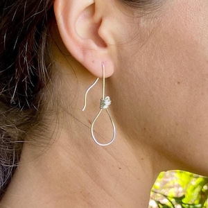 Puede incluir: Pendientes de plata con diseño de nudo. Los pendientes se muestran en la oreja de una persona.