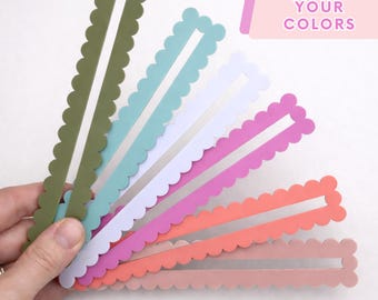 May include: A set of six long, rectangular bookmarks with scalloped edges, arranged in a fan shape. The colors include olive green, teal, white, magenta, coral, and dusty rose. A pink rectangular graphic in the corner displays the text CHOOSE YOUR COLORS.