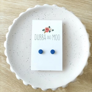 May include: A pair of small, round, blue stud earrings on a white card with the text "Dubba and Moo".