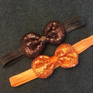 May include: Two hair ties with sparkly bows. One bow is black with gold sequins and the other is gold with gold sequins.