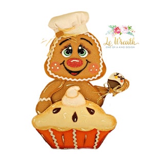Puede incluir: Un hombre de jengibre con un gorro de cocinero sostiene un peque&ntilde;o cupcake y se sienta encima de un pastel con una cobertura de crema batida.  El hombre de jengibre tiene una cara sonriente con ojos grandes y mejillas sonrosadas.  El pastel est&aacute; decorado con una corteza marr&oacute;n y un relleno blanco.  El texto "Le Wreath One-of-a-Kind Design" es visible en la esquina superior derecha de la imagen.