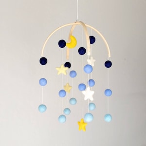 May include: A wooden baby mobile with blue, yellow, and white felt balls and stars. The mobile is suspended from a wooden hoop.