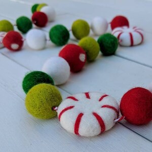 May include: A festive garland featuring felt balls and peppermint-shaped ornaments. The garland includes red, green, white, and yellow-green balls, and white ornaments with red stripes. Perfect for holiday decor.