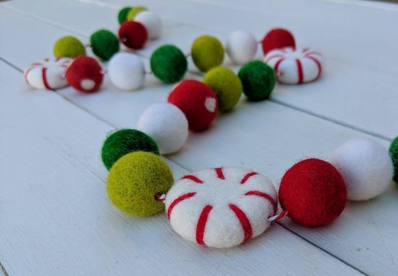May include: A festive garland featuring felt balls and peppermint-shaped ornaments. The garland includes red, green, white, and yellow-green balls, and white ornaments with red stripes. Perfect for holiday decor.
