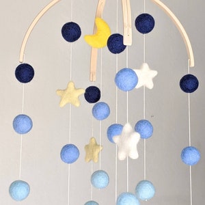 May include: A wooden baby mobile with blue, yellow, and white felt balls and stars. The mobile is suspended from a wooden arch.