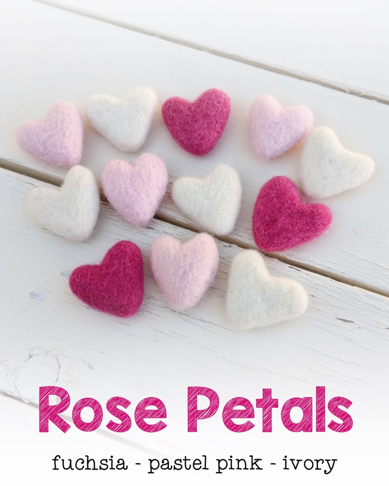 May include: A collection of felt hearts in three colors: fuchsia, pastel pink, and ivory. The hearts are arranged in a circle on a white wooden surface.