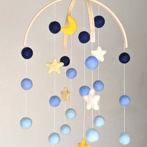 May include: A wooden baby mobile with blue, yellow, and white felt balls and stars. The mobile is suspended from a wooden arch.
