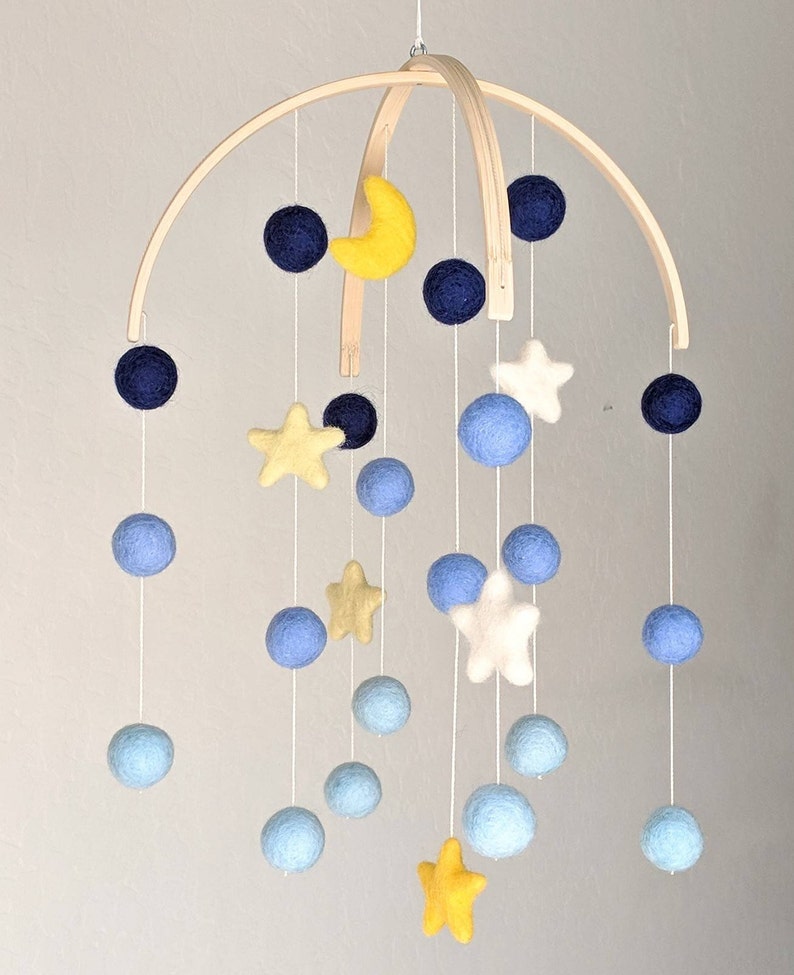 May include: A wooden baby mobile with blue, yellow, and white felt balls and stars. The mobile is suspended from a wooden arch.