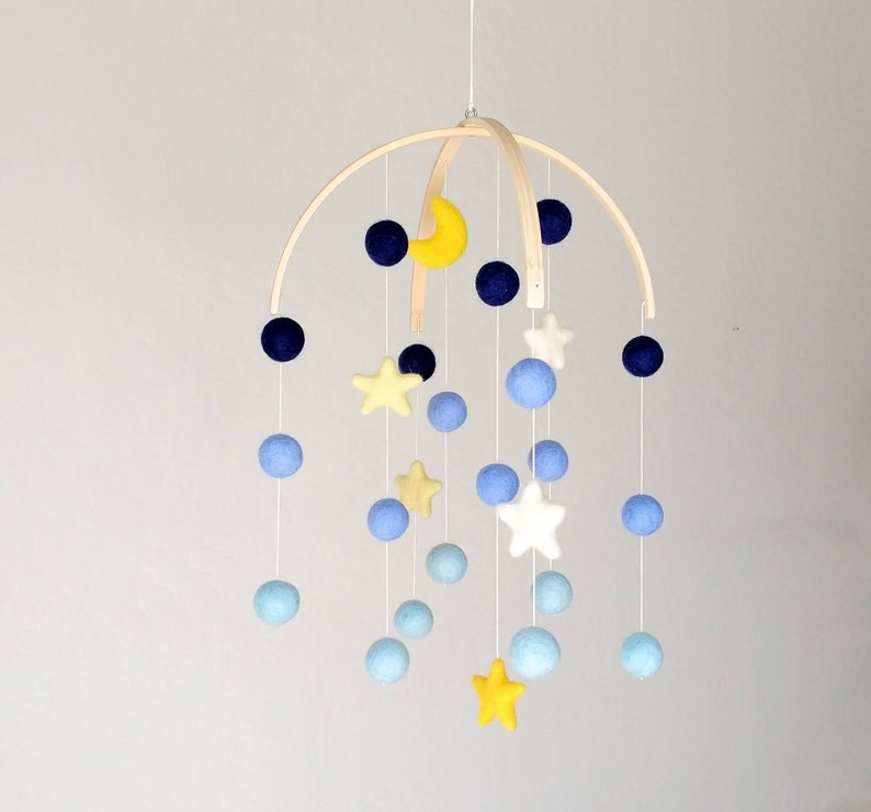 May include: A wooden baby mobile with blue, yellow, and white felt balls and stars. The mobile is suspended from a wooden hoop.