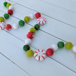 May include: A festive garland featuring red, green, white, and yellow felt balls and peppermint candies. The garland is strung together with red and white twine, perfect for holiday decorations. The felt balls are in various sizes.