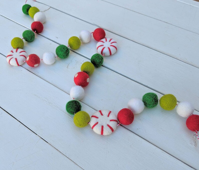 May include: A festive garland featuring red, green, white, and yellow felt balls and peppermint candies. The garland is strung together with red and white twine, perfect for holiday decorations. The felt balls are in various sizes.