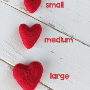 May include: Three red felt hearts of different sizes on a white wooden background. The hearts are labeled "small", "medium", and "large".