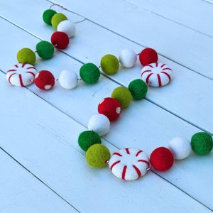 May include: A festive garland featuring red, white, green, and yellow felt balls and peppermint-shaped ornaments. The garland is strung on a red and white twine, perfect for holiday decorations. The felt balls are approximately 1 inch in diameter.