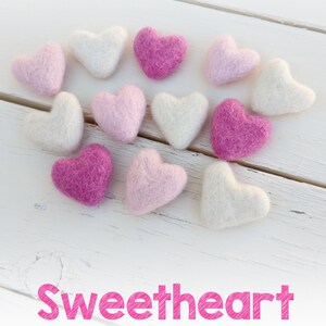 May include: A collection of felt hearts in various shades of pink and ivory. The hearts are arranged in a heart shape on a white wooden surface. The text "Sweetheart" is written in pink below the hearts. The text "bright pink - pastel pink - ivory" is written below the word "Sweetheart".