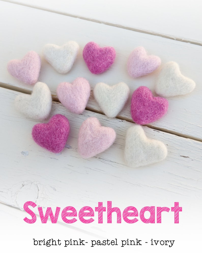 May include: A collection of felt hearts in various shades of pink and ivory. The hearts are arranged in a heart shape on a white wooden surface. The text "Sweetheart" is written in pink below the hearts. The text "bright pink - pastel pink - ivory" is written below the word "Sweetheart".