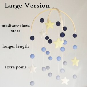 May include: A wooden baby mobile with a white, yellow, and blue color scheme. The mobile features felt stars and pom-poms hanging from a wooden hoop.