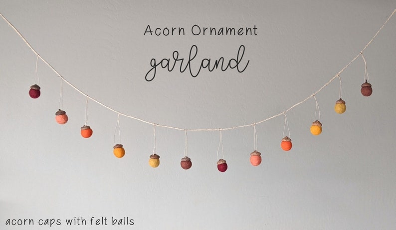 May include: A garland of felt acorn ornaments in shades of red, orange, and yellow. The acorns are strung on a white twine and the text "Acorn Ornament garland" is written above the garland. The text "acorn caps with felt balls" is written below the garland.