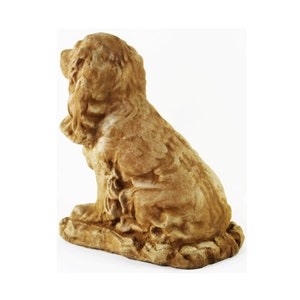 May include: A brown ceramic sculpture of a sitting dog. The dog has long, flowing ears and a tail curled around its legs. The sculpture is detailed with realistic features and a textured surface.