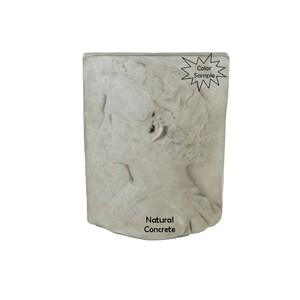 May include: A gray concrete wall sculpture of a woman's face in profile. The sculpture is mounted on a wall and has a natural concrete finish. The text "Natural Concrete" is printed below the sculpture.