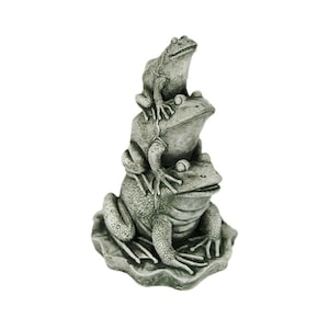 May include: A stack of three gray ceramic frogs, with the smallest frog on top, sitting on a leaf-shaped base.