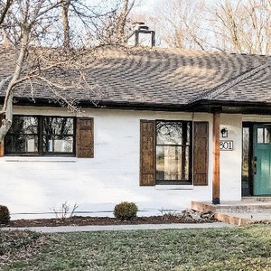 May include: Exterior view of a house with white painted brick, brown shutters, and a teal front door. The house number "801" is visible above the door. The roof is dark brown, and the yard has grass and small bushes.