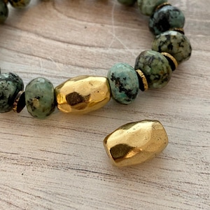 Op de afbeelding: Een armband met turquoise en goudkleurige kralen. De armband heeft een mix van ronde en onregelmatig gevormde kralen. De gouden kralen hebben een gehamerde textuur. De armband ligt op een lichtgekleurd houten oppervlak.
