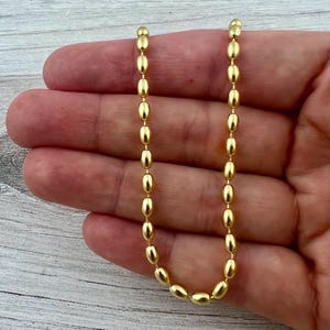 May include: A gold chain necklace with oval-shaped links. The chain is laying on a hand.