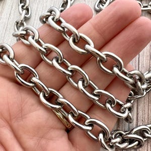 May include: A silver-toned metal chain featuring a series of interconnected oval links. The chain has a polished, reflective surface and is constructed from uniform, smooth, rounded links that create a continuous, flexible, and durable design.