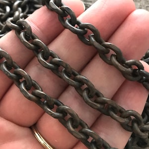 May include: Close-up of a dark grey metal chain with oval links. The chain has a textured finish and appears to be antique or vintage. The chain is likely used for jewellery or craft projects.