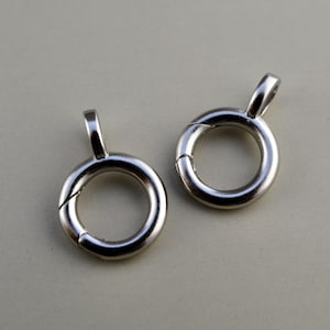 May include: Two silver-toned metal spring rings, each featuring a circular loop with a small attached bail. The rings have a smooth, polished finish and a visible seam where the spring mechanism allows the circular part to open and close securely.