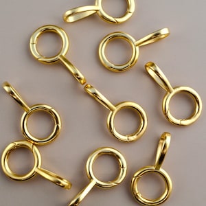 May include: Gold-colored metal lobster clasps with a circular ring and a small handle. The clasps are shown scattered on a neutral background. These clasps are used for jewelry making and other crafting projects.