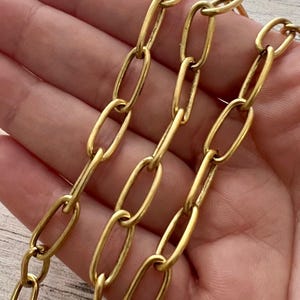 May include: Close-up of a gold-colored chain with large oval links. The chain is made of metal and has a shiny finish. The links are connected in a repeating pattern, creating a bold and eye-catching design.