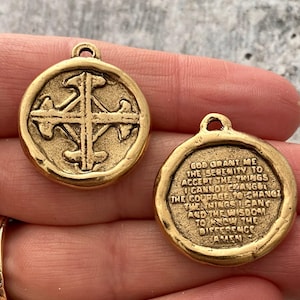 Puede incluir: Dos colgantes redondos de color oro antiguo. Uno presenta un diseño de cruz, mientras que el otro tiene la inscripción "Dios, concédeme la serenidad para aceptar las cosas que no puedo cambiar..." Los colgantes tienen un lazo en la parte superior.