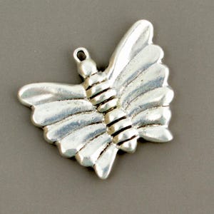 May include: A silver-colored butterfly charm with detailed wing patterns and a loop at the top for attaching to jewelry or other crafts. The butterfly has a textured appearance and is set against a gray background.