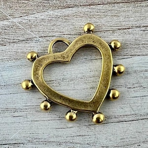 May include: A brass-toned metal heart charm featuring an open center and a series of small, smooth spherical beads attached to the outer edge. The charm includes a small circular loop at the top for attachment, with a weathered, antique finish.