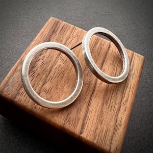 Op de afbeelding: Twee cirkelvormige zilverkleurige ringen met een gladde, gepolijste afwerking. De ringen hebben een eenvoudig, doorlopend bandontwerp met een consistente dikte, wat zorgt voor een metaalachtige glans en een afgerond profiel voor elk stuk.
