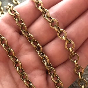 May include: Close-up of several strands of antique brass-colored chain. The chain links are oval-shaped and interlocked, creating a textured surface. The chains are displayed against a blurred background, highlighting the intricate details of the jewelry.
