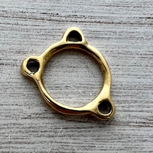 Könnte beinhalten: Ein goldfarbener Metallring mit drei gleichmäßig verteilten kreisförmigen Befestigungspunkten. Der Ring ist kreisförmig mit einer glatten, polierten Oberfläche. Die Befestigungspunkte sind klein und abgerundet, mit einem Loch in der Mitte.