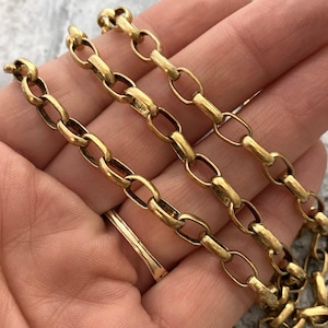 May include: Close-up of a gold-colored chain necklace with oval links. The chain is made of metal and has a vintage or antique appearance. The links are connected in a repeating pattern, creating a classic jewelry design.