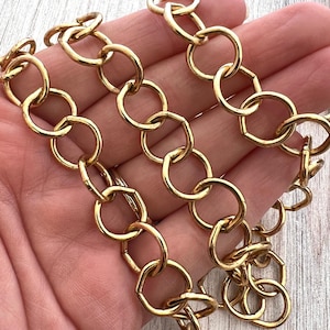 May include: Close-up of a gold-colored chain with large, round links. The chain is made of metal and has a shiny finish. The links are connected in a repeating pattern, creating a bold and eye-catching design. The chain is likely used for jewelry or accessories.