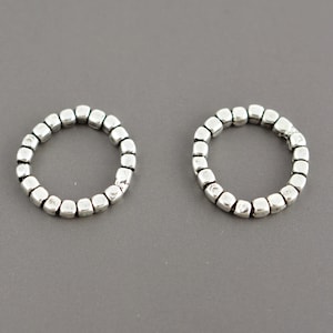 May include: Two circular rings constructed from small, individual silver-toned metallic cube beads. Each ring features a uniform, repeating pattern of these square-shaped components linked together to form a continuous, flexible circular band.