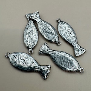 May include: Five silver-toned metal fish charms with a textured, weathered finish. Each fish-shaped pendant features a small, clear embedded rhinestone eye and two circular loops at the head and tail ends for attachment to jewelry or craft projects.