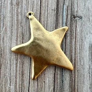 Può includere: Un ciondolo a forma di stella a cinque punte con finitura oro metallizzato e una texture superficiale liscia e leggermente irregolare. La stella presenta un piccolo occhiello circolare sulla punta superiore per l'aggancio, come gioiello.