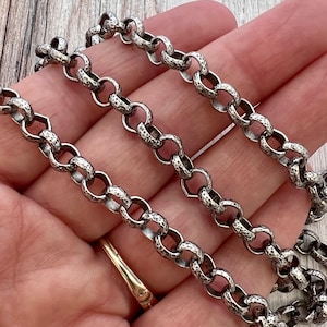 May include: A silver-toned metal chain necklace featuring a series of interconnected round links. Each individual link displays a distinct hammered, textured surface finish, creating a consistent pattern throughout the entire length of the chain.