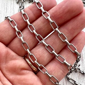 May include: Close-up of three silver-colored chain necklaces with oval links. The chains are displayed against a warm-toned background. The links are uniform in size and shape, creating a consistent pattern. The chains are likely jewelry.