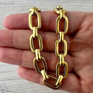 May include: A gold-colored chain bracelet with oval links. The bracelet is made of metal and has a clasp closure. The links are connected in a repeating pattern, creating a stylish accessory.