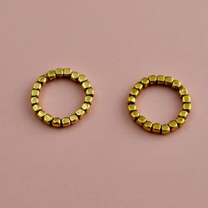 May include: Two circular rings constructed from small, metallic gold-toned cube-shaped beads. Each ring features a continuous, uniform arrangement of these individual square-edged components, creating a textured, beaded appearance in a circular form.