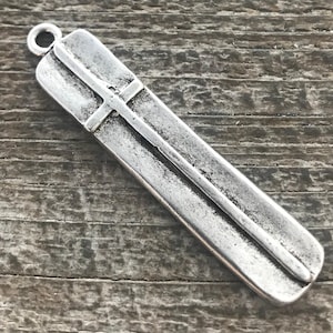 Puede incluir: Colgante rectangular plateado con diseño de cruz. Tiene un lazo en la parte superior para sujetarlo a una cadena o cordón. La superficie presenta un aspecto texturizado y envejecido.